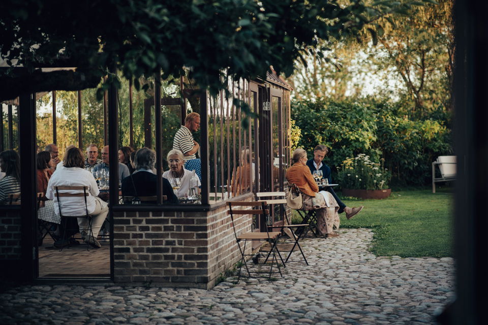 Gäster som äter och dricker i ett växthus i anslutning till restaurangen på Kullabergs Vingård.