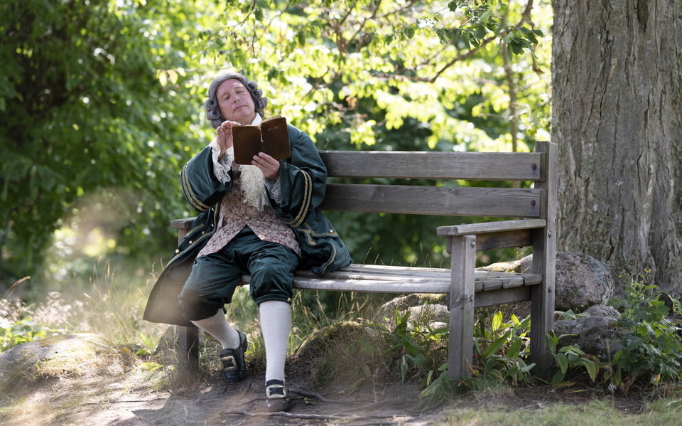 Carl von Linné sitter på en bänk och läser en bok