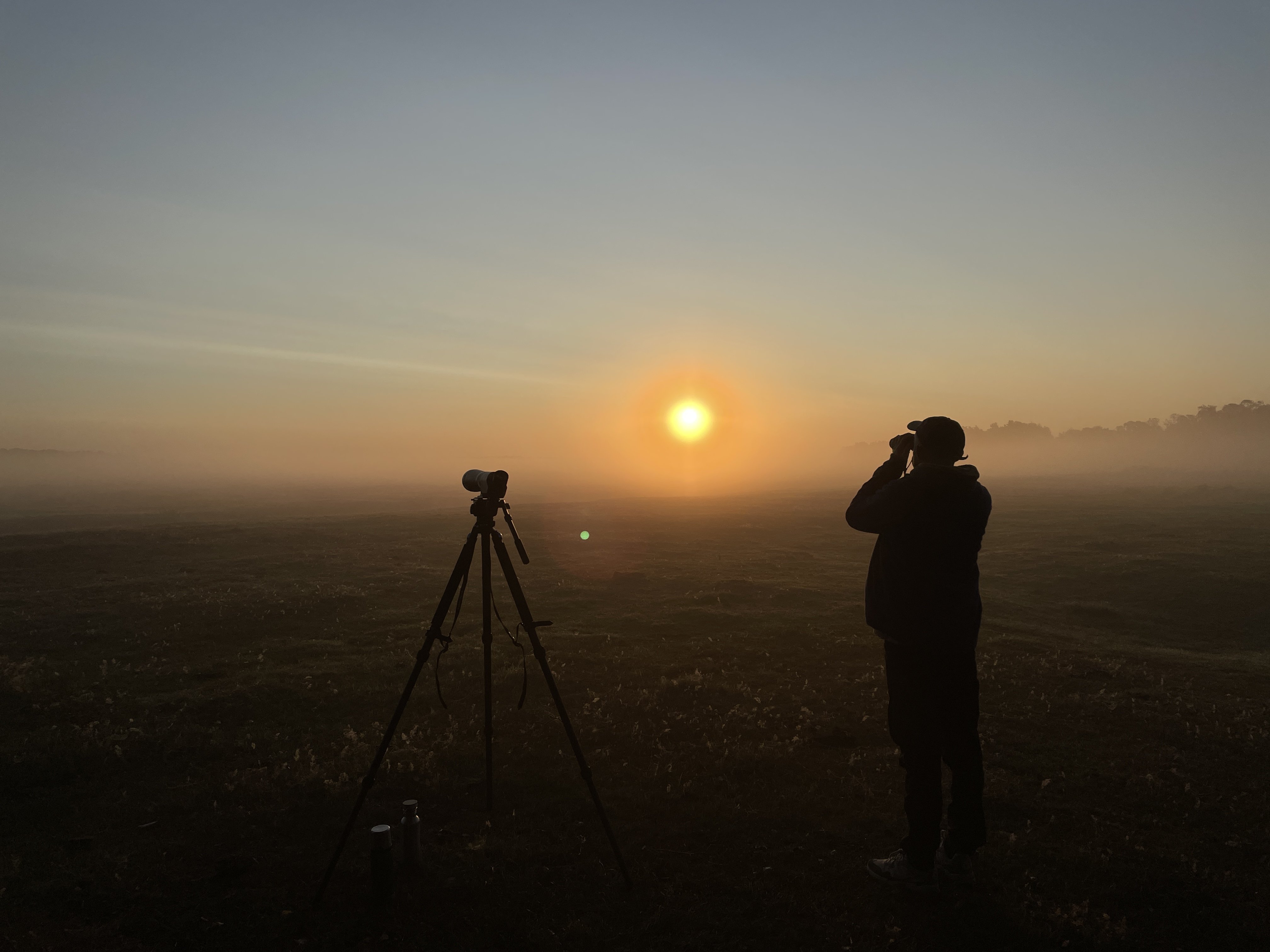 Fågelskådare kikar mot horisonten på en ljunghed en dimmig soluppgång.