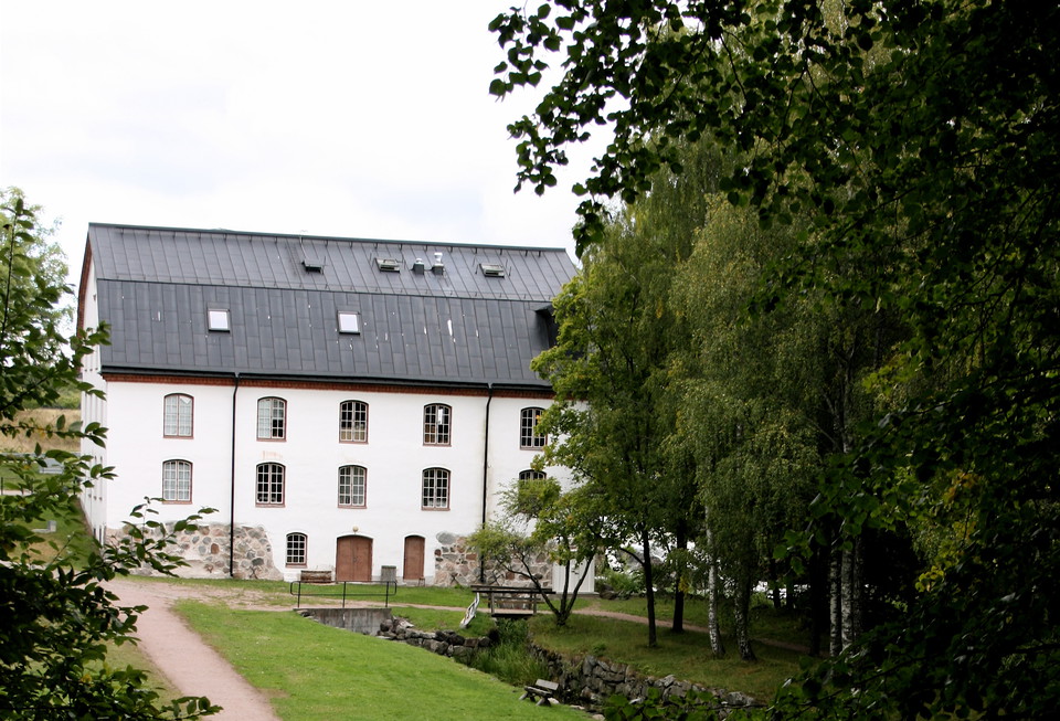 Ett mycket stort vitt stenhus med många fönster med en skogsdunge i förgrunden.