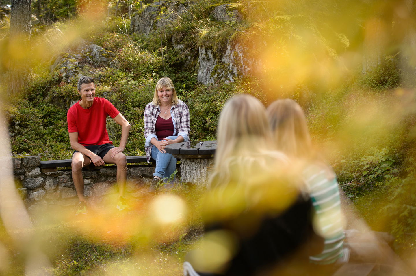 Ett par sitter vid bänken efter stigen. I förgrunden står två tjejer.