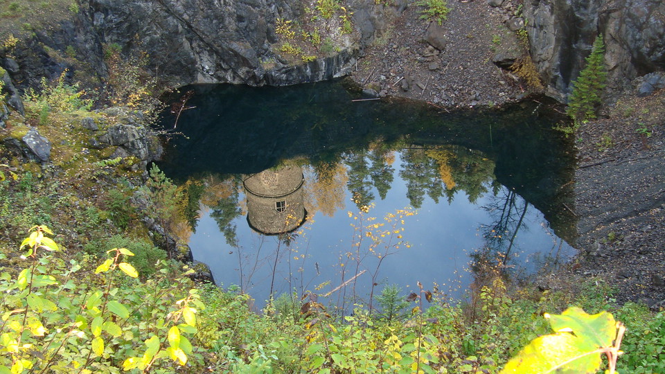 En lave byggd av slaggsten speglar sig i ett dagbrott fyllt av vatten.