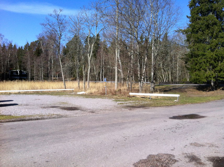 Vid sidan av en asfalterad väg finns en grusad parkeringsplats med ett lågt räcke på sidorna.