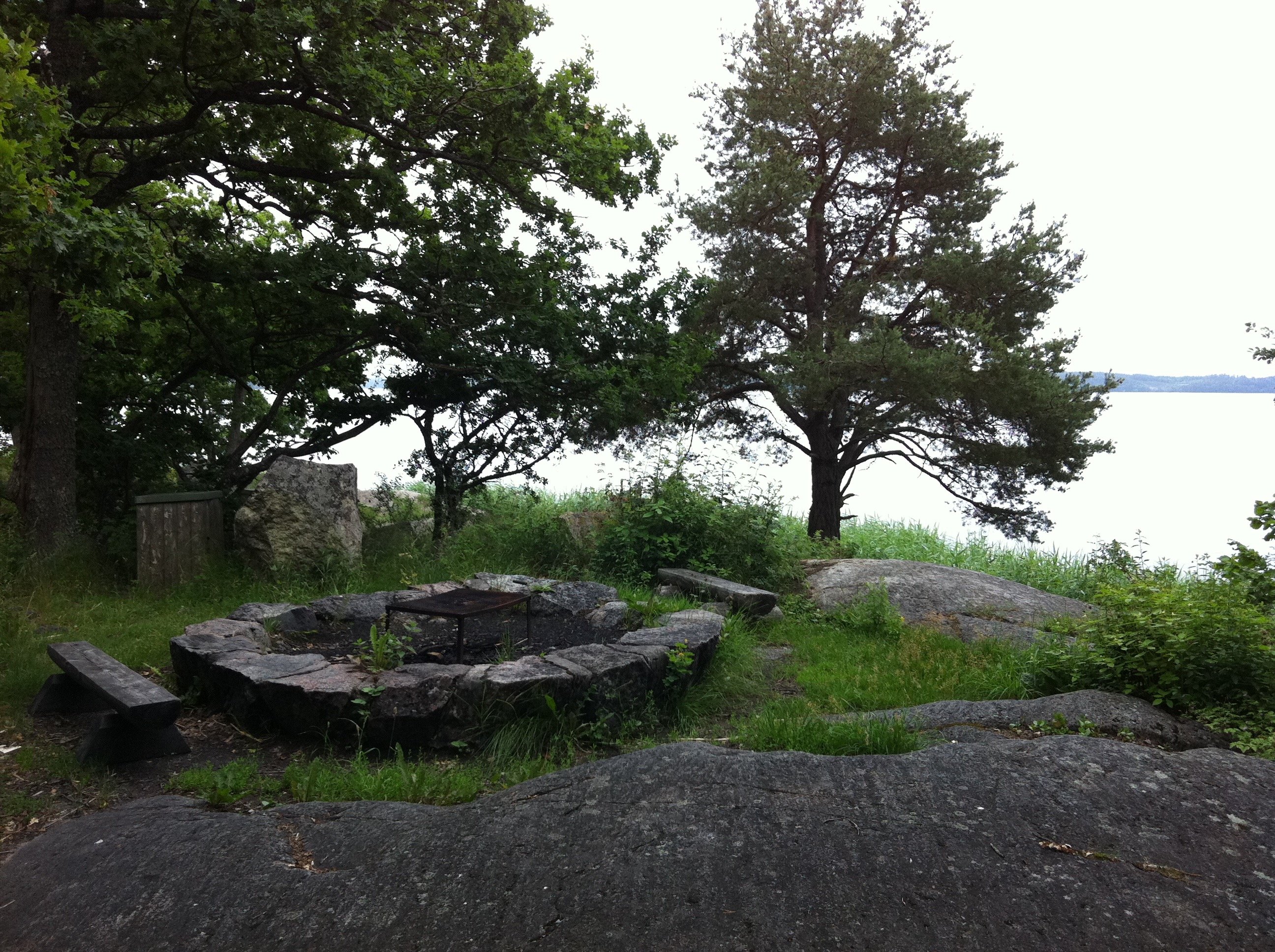 En grillplats med galler och sittbänkar vid en stenhäll nära vattnet.