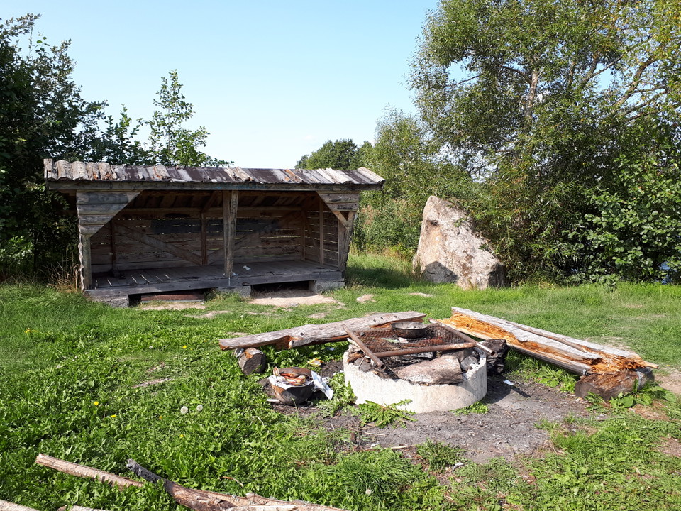Ett vindskydd i trä, en rund grillplats med två bänkar intill.