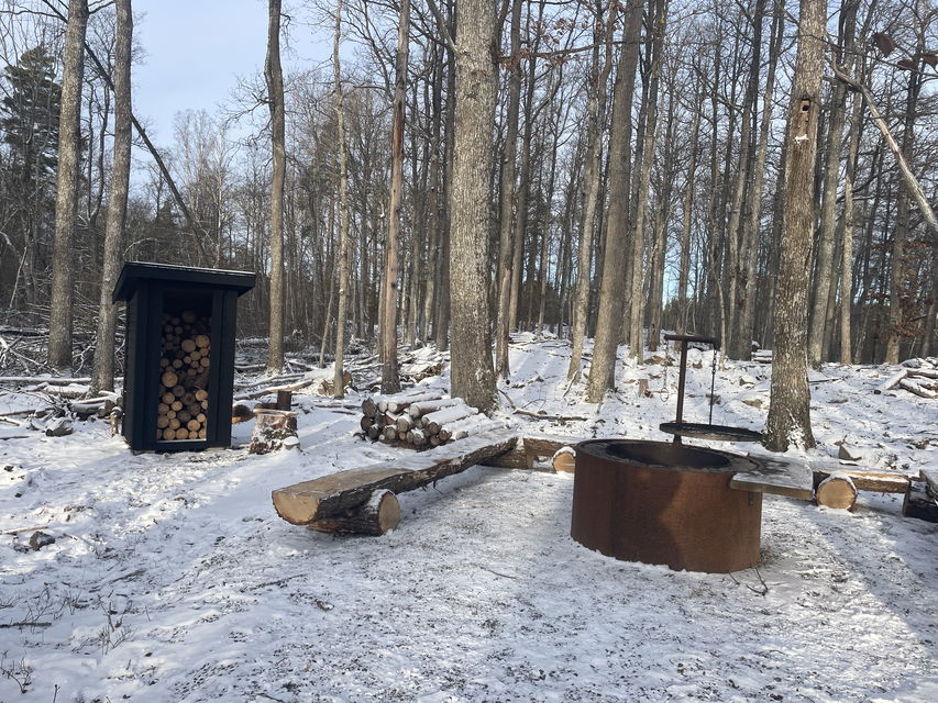 Grillplats med sittstockar och vedförråd i snöigt landskap