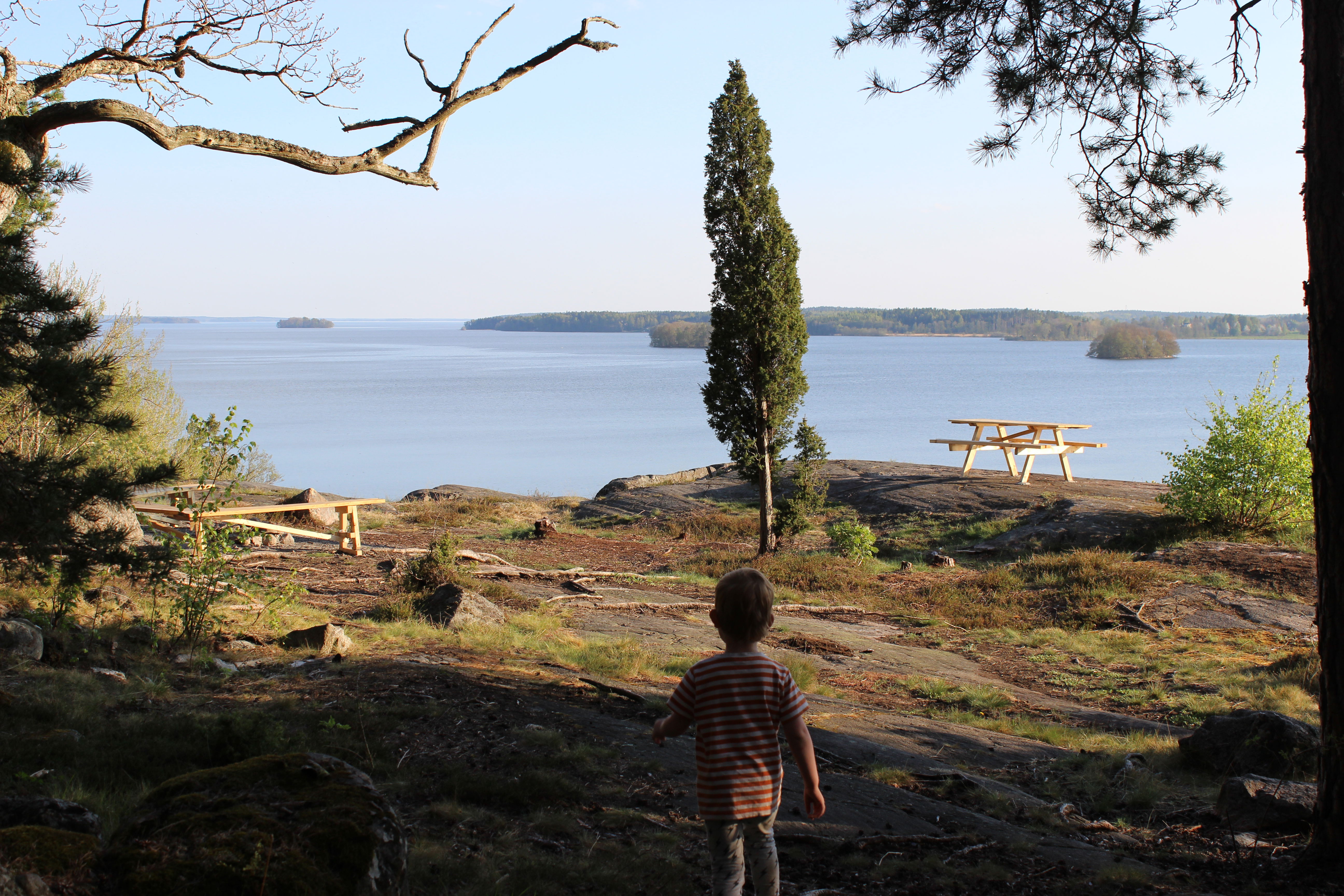 Ett barn går ut på klippor vid vattnet. På klipporna står en bänk och ett bänkbord.