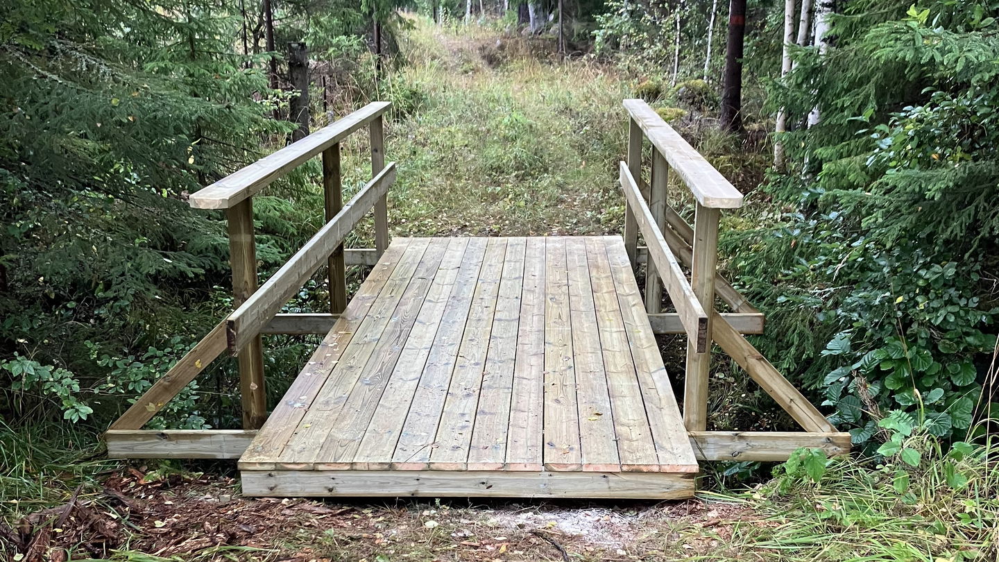 En bro av trä som går över dike vid vandringsled