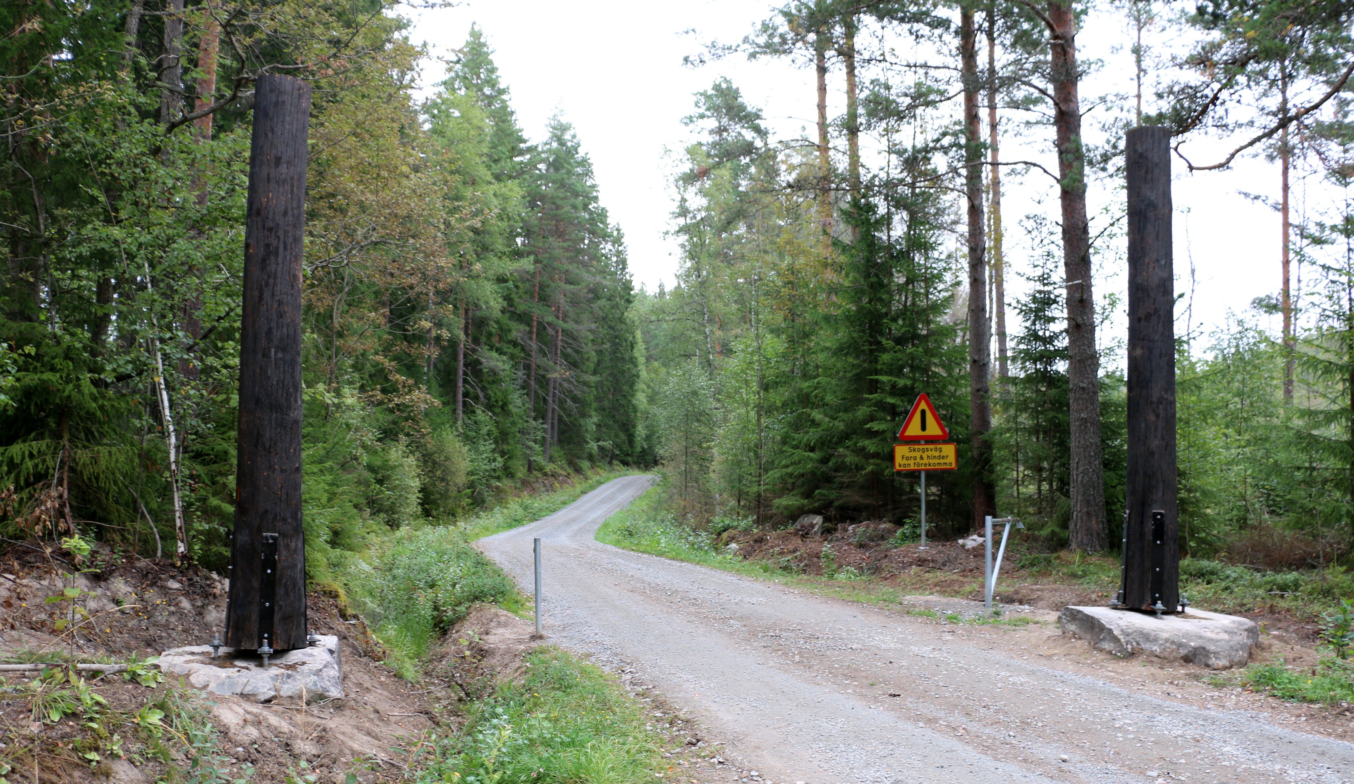 Grusväg som leder in i skogen. Vid infarten finns en vägbom och en varningsskylt.