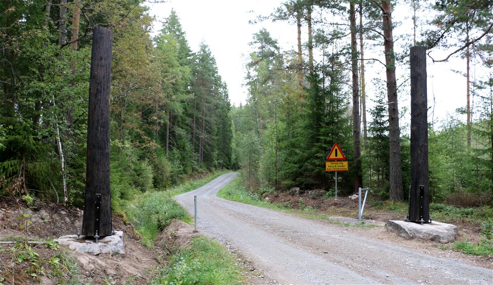 Grusväg som leder in i skogen. Vid infarten finns en vägbom och en varningsskylt.