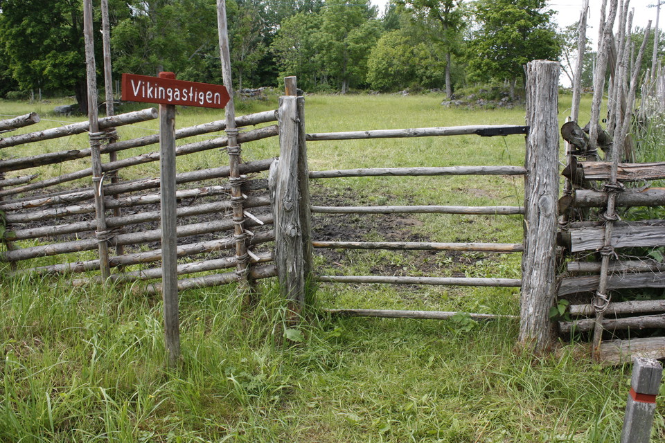 En stig leder fram till en grind vid en gärdesgård. En vägvisare står vid grinden.