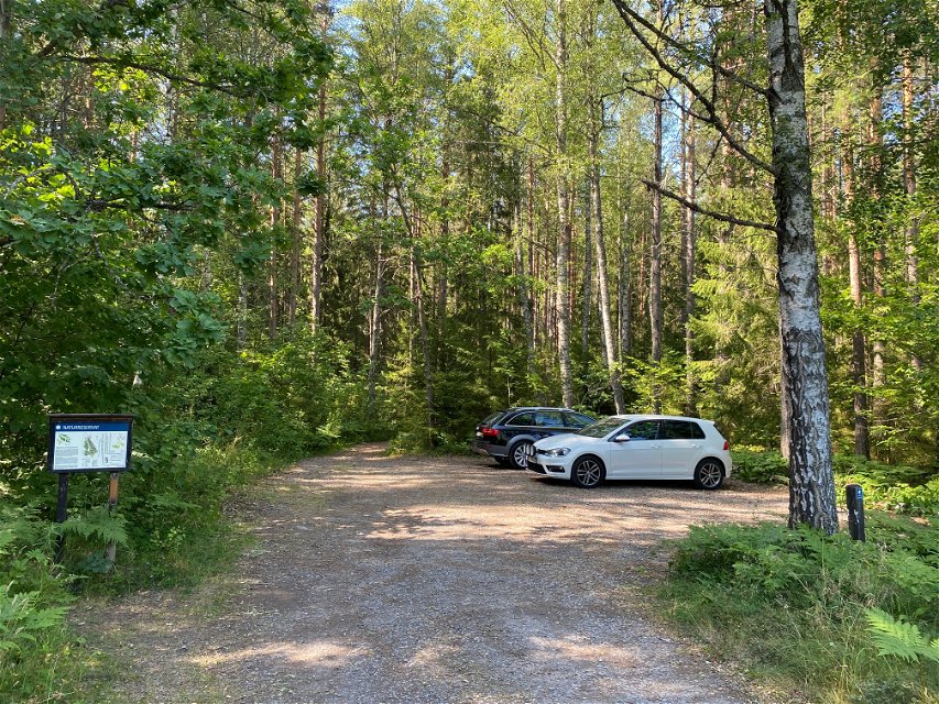 Två bilar står på en grusad parkeringsplats med skog runtom.