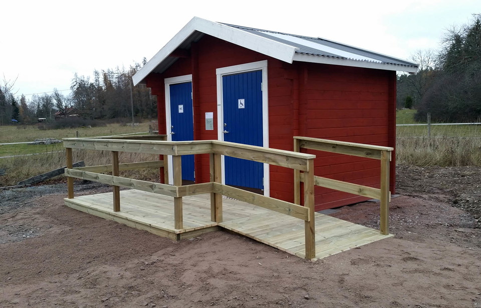 Röd byggnad med två blåa dörrar och en rullstolsramp med räcke.