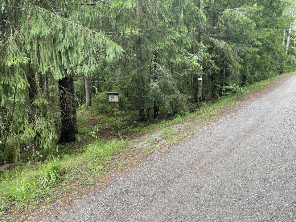 Informationstavla vid stig inne i en skog. Reservatsmarkering på ett träd.