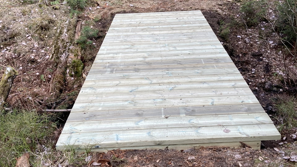 En bro av trä som går över dike vid vandringsled