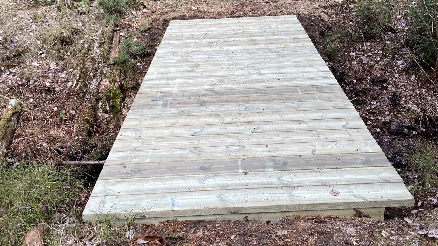 En bro av trä som går över dike vid vandringsled