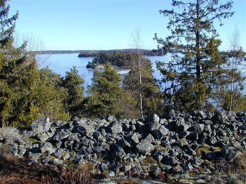 Uppe på en höjd ligger många större stenar. Från platsen har man utsikt över skog, sjön Mälaren och små öar.