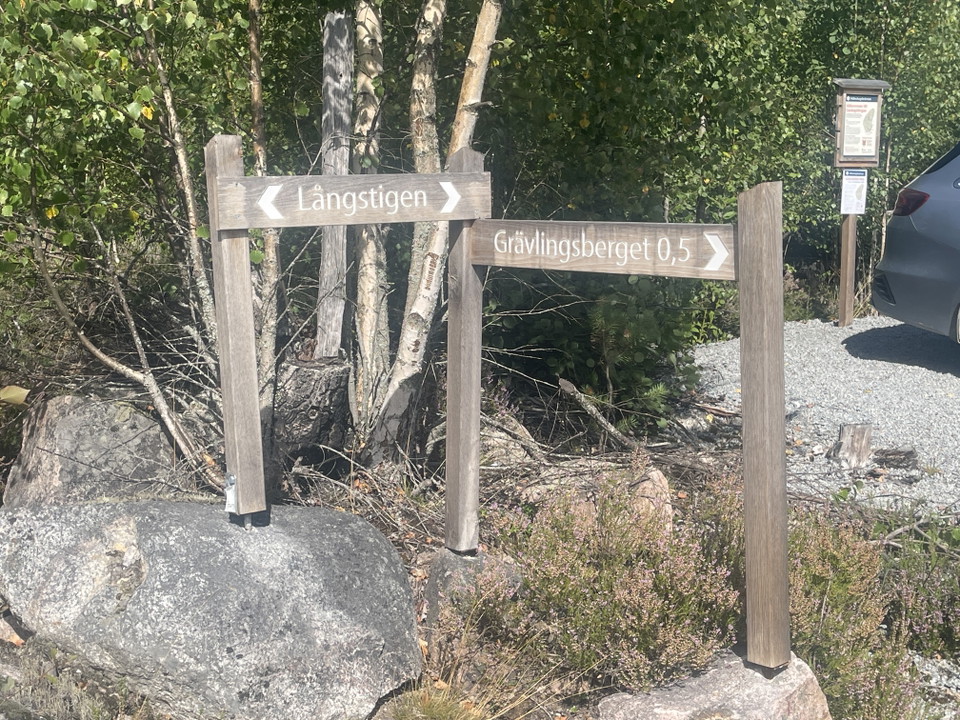 Parkering med informationsskylt och vägvisning mot stigar.