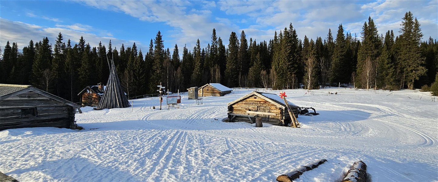 Små hus som ligget vid ett skogsbryn. Det ligger snö på marken