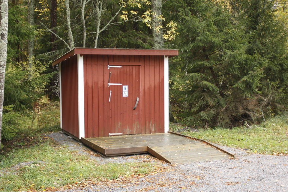 Ett utedass med ramp står vid parkeringens kant.