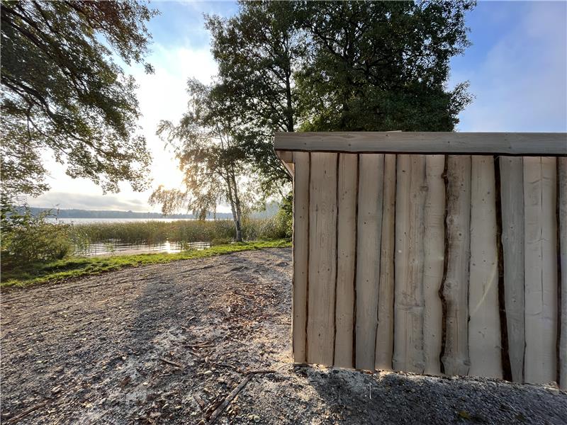 bild på vindskydd, i bakgrunden syns träd och sjön.