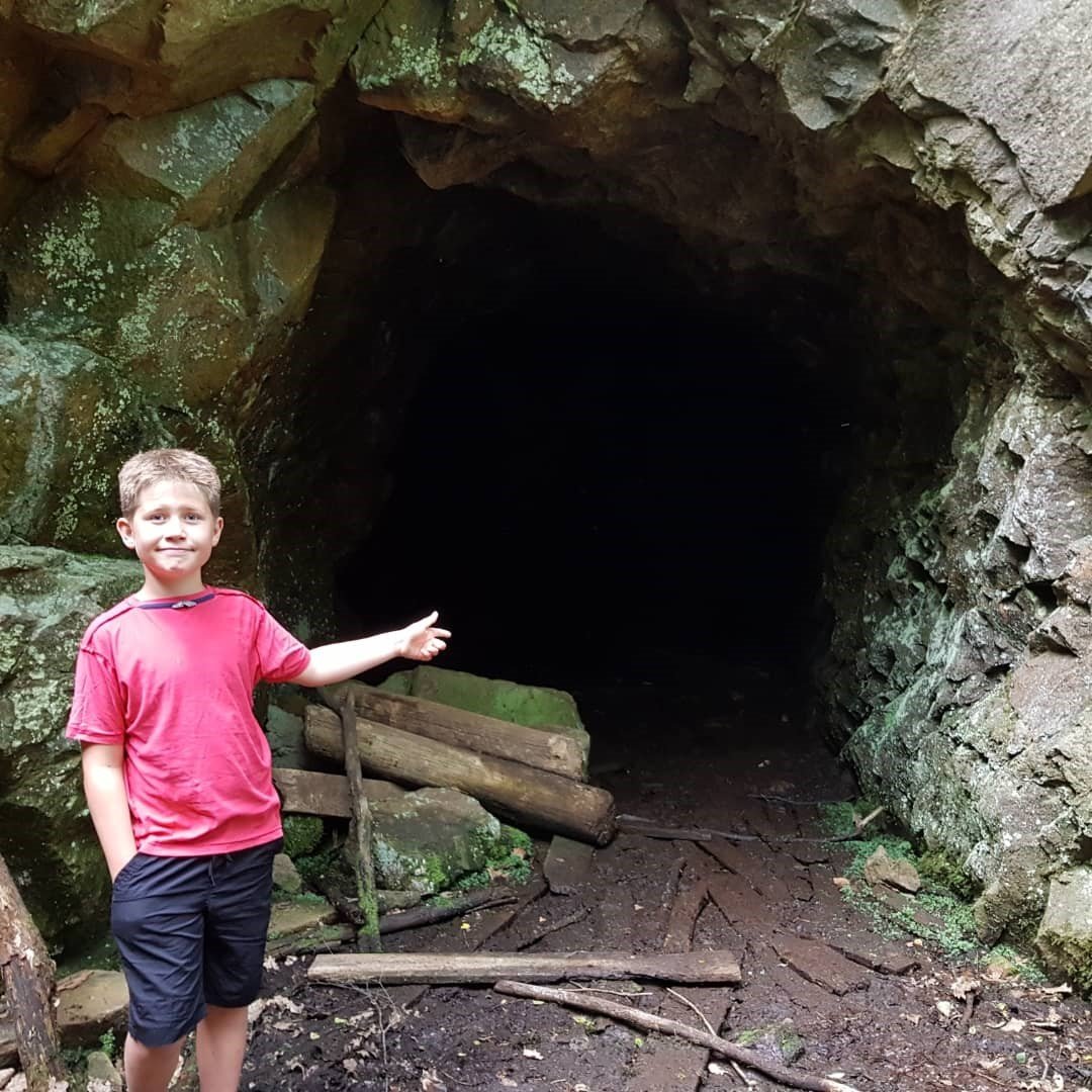 En pojke står utanför grottan och pekar in i mörkret