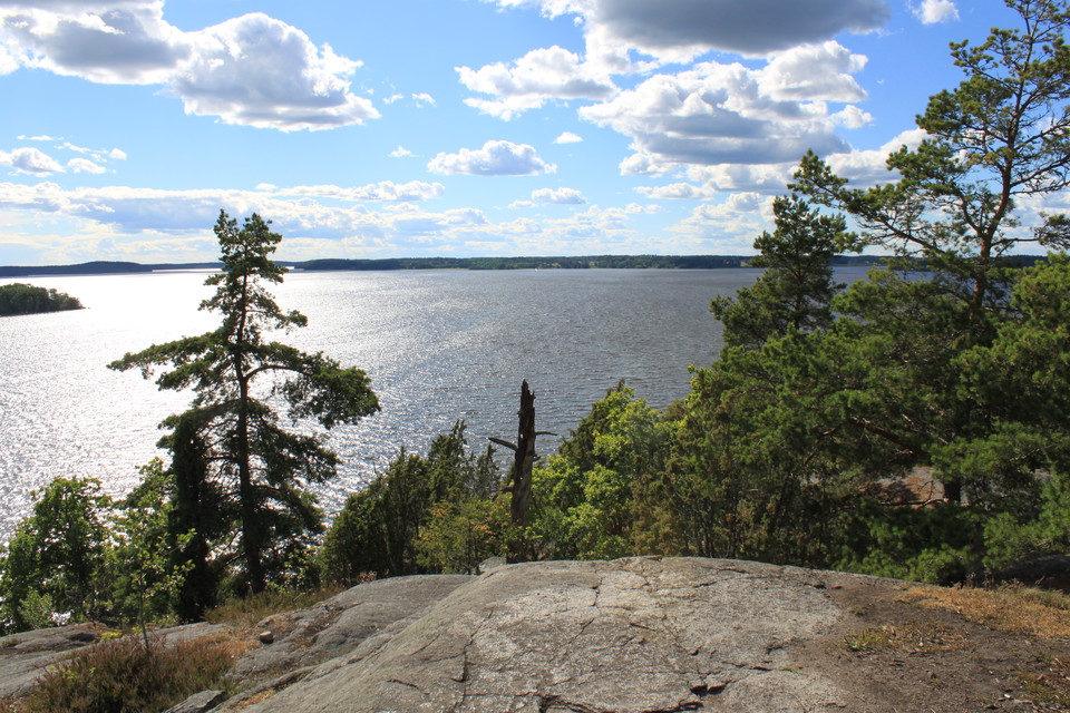Från ett högt berg har man utsikt över vatten och skogen i slänten nedanför berget.