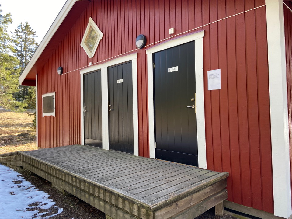 Ett rött hus med tre svarta dörrar och en ramp och plattform i trä framför