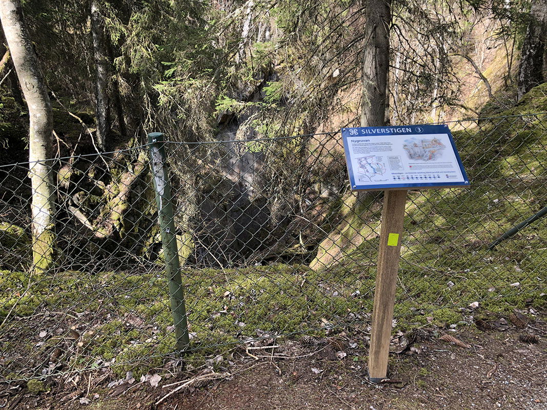 Informationstavla vid stort inhägnat gruvhål.