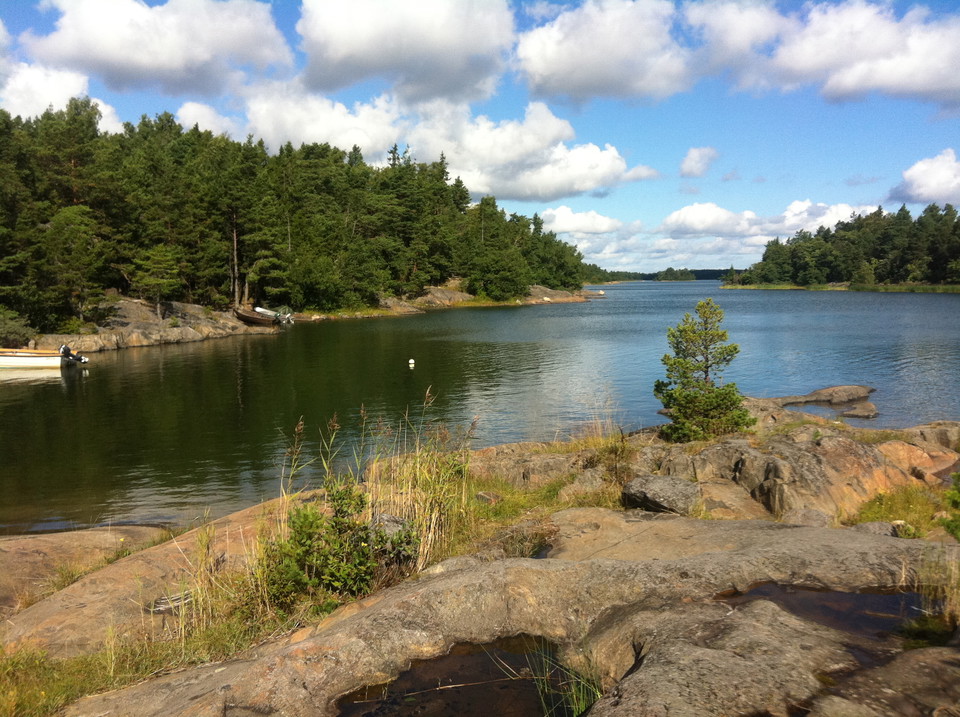 En havsvik med stenhällar och skog. Två mindre båtar är förankrade vid vattnet. 