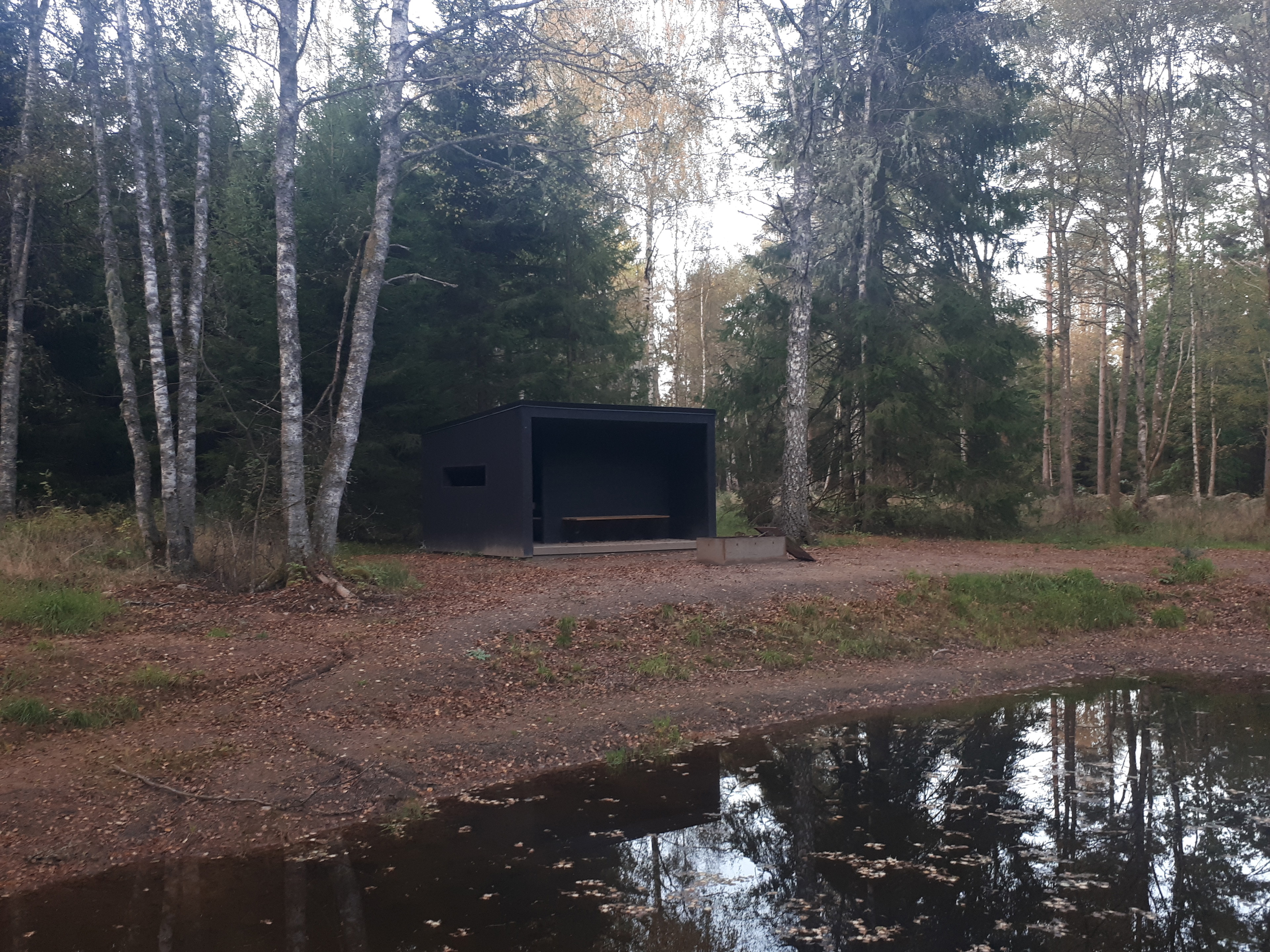 Ett vindskydd med vatten framför och skog bakom.