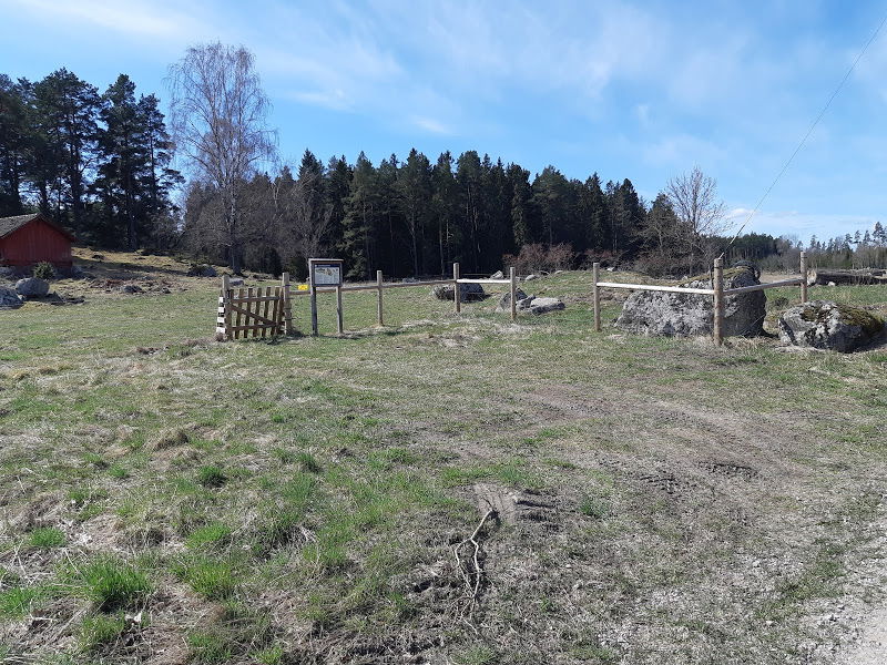 En öppen yta med grästuvor och något lerig mark. Runt parkeringen står ett stängel in till en beteshage och en informationsskylt.