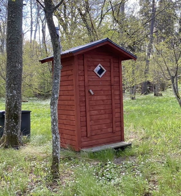 En liten toalett med ett litet rombiskt fönster i dörren. Utanför dörren finns ett trappsteg.