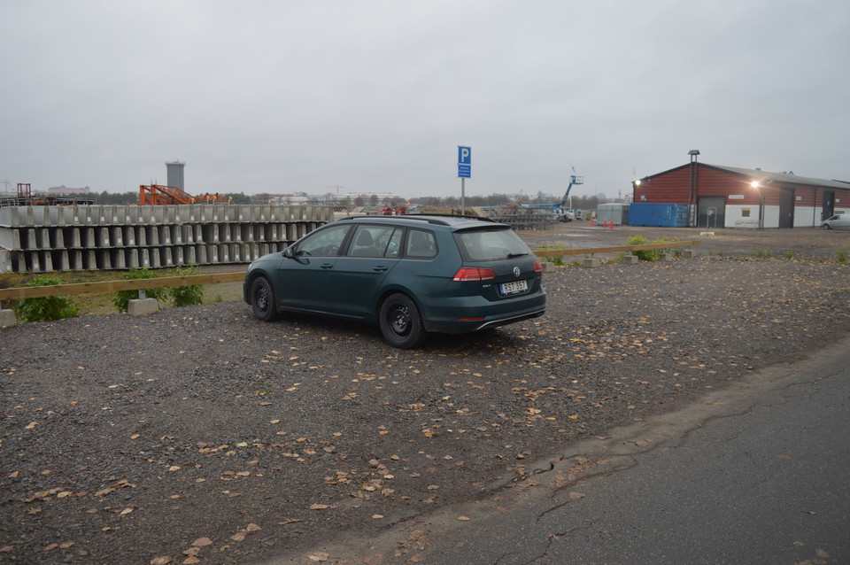 Vid en asfalterad väg finns en grusad parkeringsplats. En bil står på parkeringsplatsen.