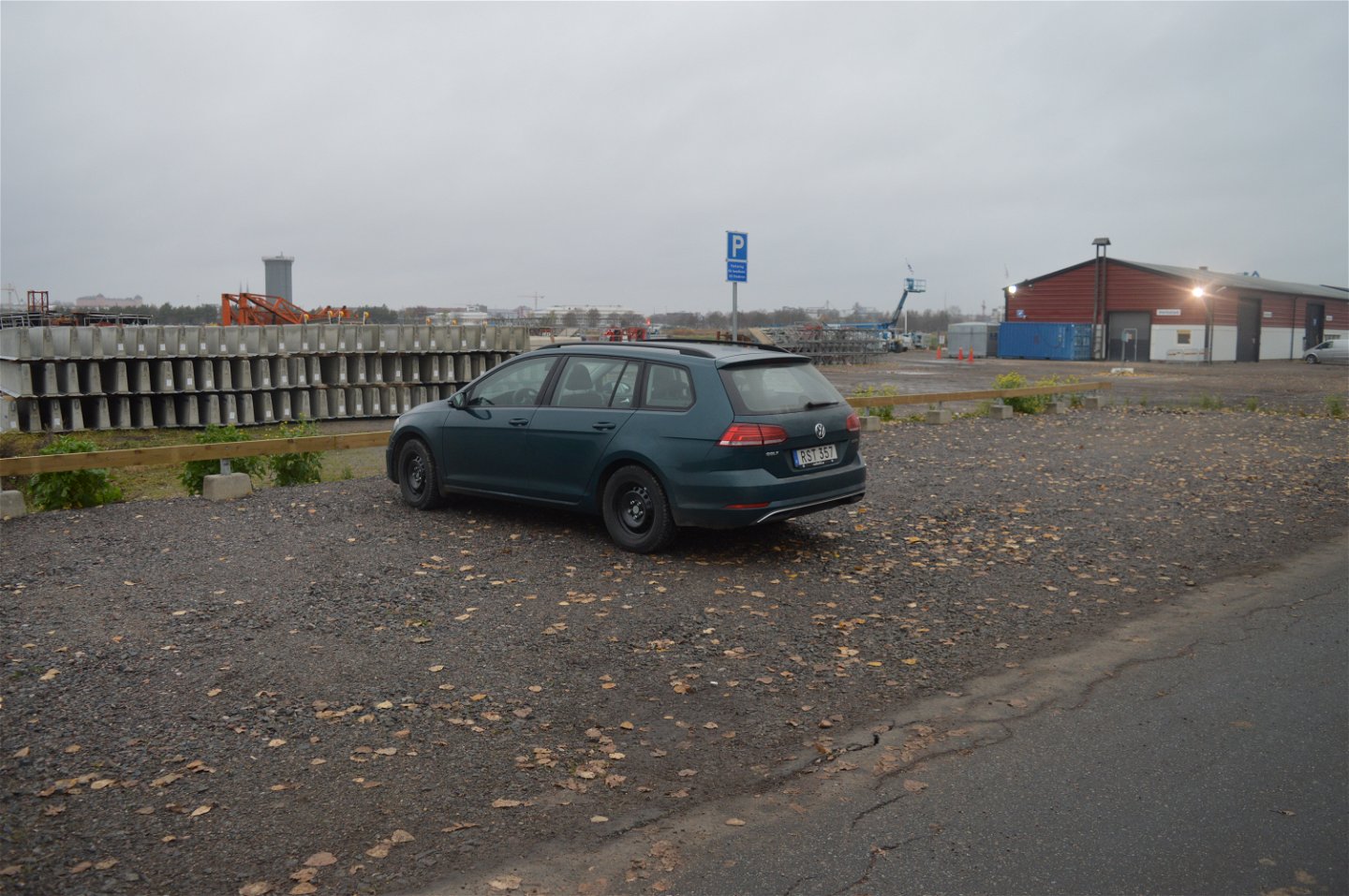 Vid en asfalterad väg finns en grusad parkeringsplats. En bil står på parkeringsplatsen.
