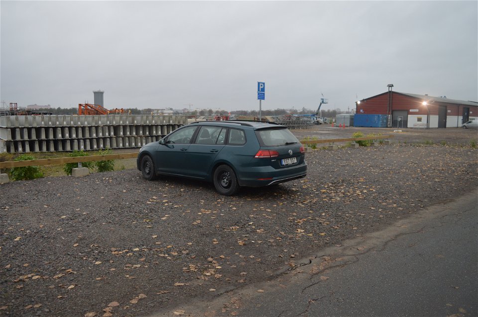 Vid en asfalterad väg finns en grusad parkeringsplats. En bil står på parkeringsplatsen.