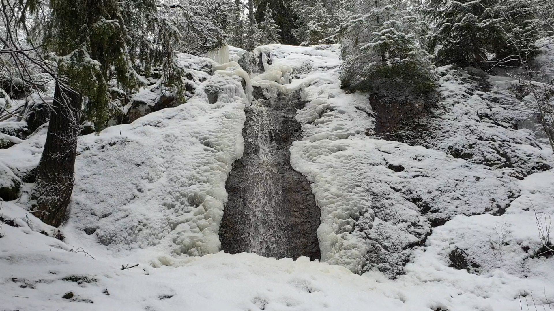Vattenfall i barrskog i ett snöigt landskap.