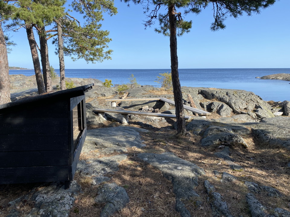 Vedförråd, bänkar och grillplats på klippor med utsikt över havet.