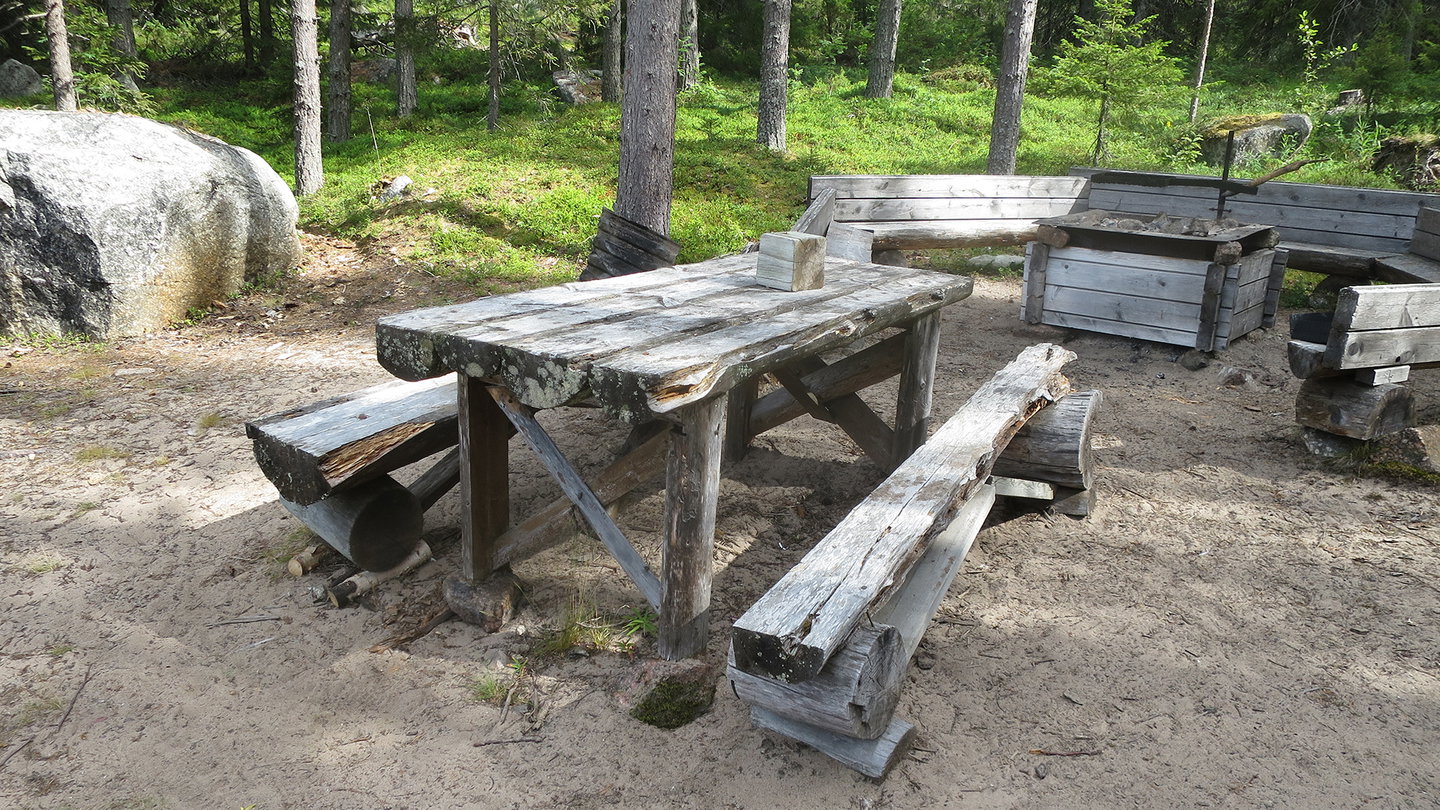 Ett sandigt område med ett bord med två bänkar och en eldstad bakom.