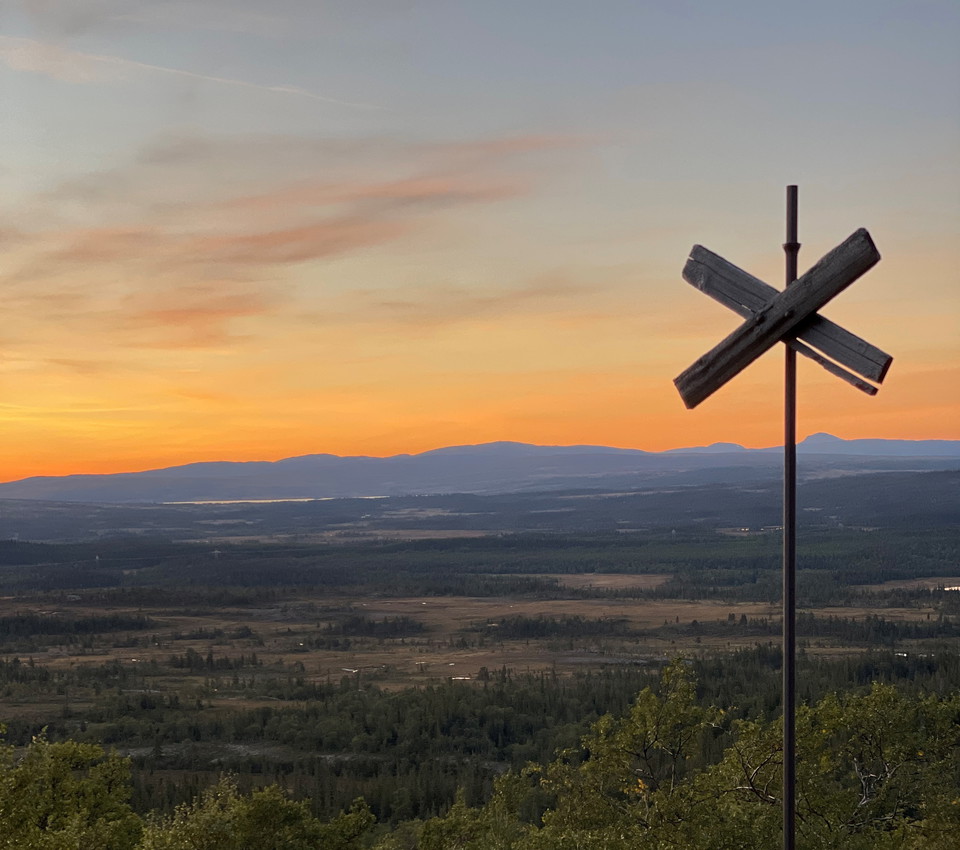 Solnedgång över ett fjäll med ett ledkryss i förgrunden