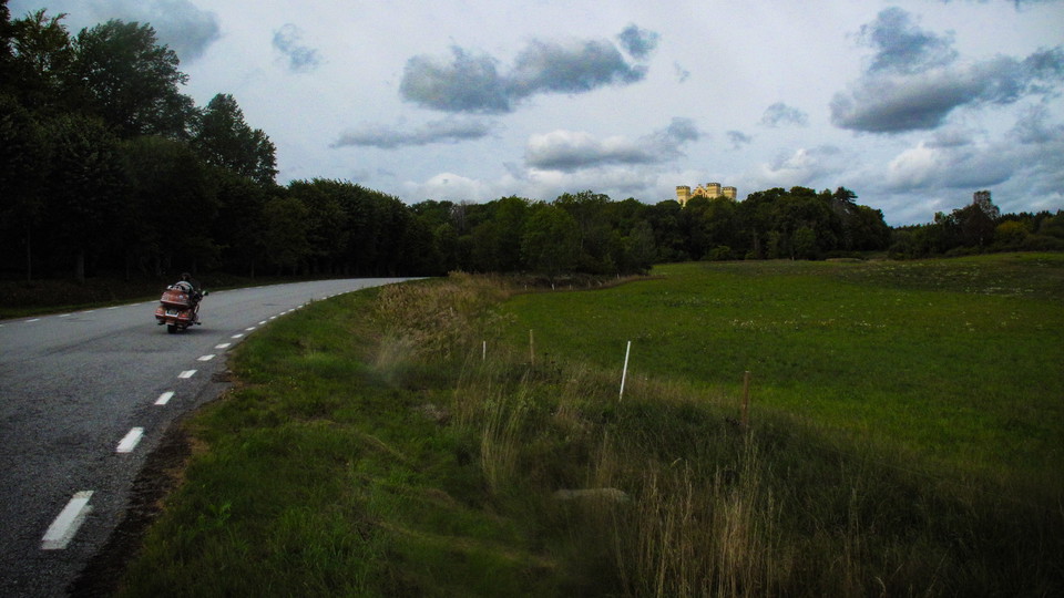 Landsvägen på Bogesundslandet med en motorcykel. Över träden sticker Bogesunds Slott upp.