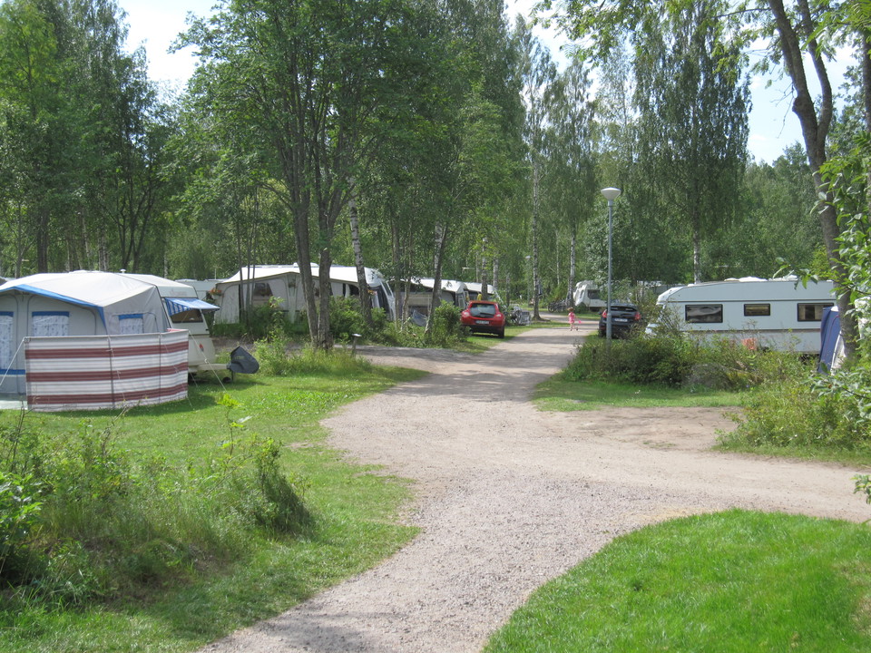 Flera husbilar är parkerade på båda sidor av en grusad väg. 