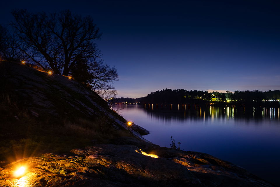 Skymningsbild över Brunnsviken med facklor runt sjön.