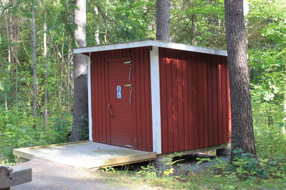 En tillgänglighetsanpassad torrtoalett med en bred träramp med kanter framför.