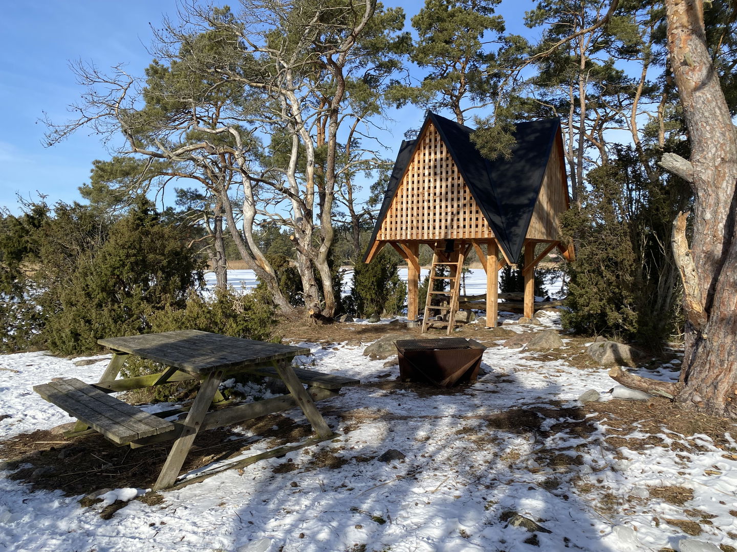 Vindskydd, grill och bänkbord. Solig vinterdag med snö