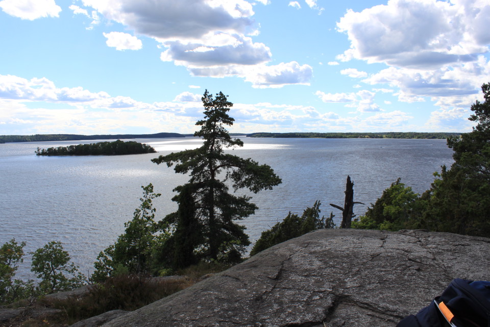 Från ett högt berg har man utsikt över vatten och skogen i slänten nedanför berget.