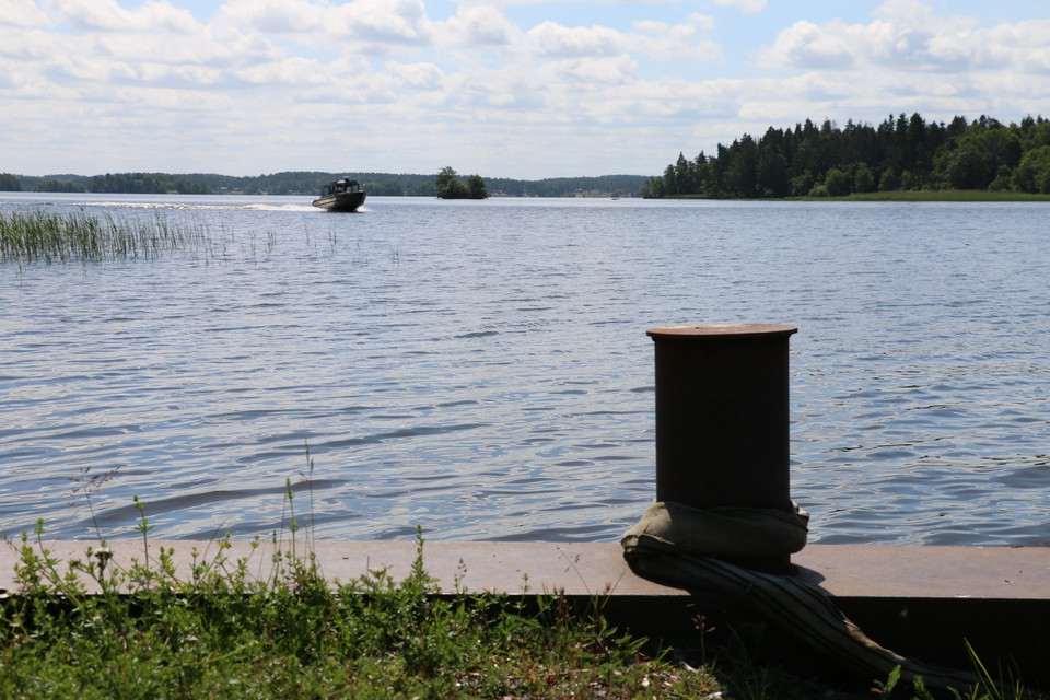 Järnstolpe för förtöjning av båt. På vattnet kommer en motorbåt in mot land.