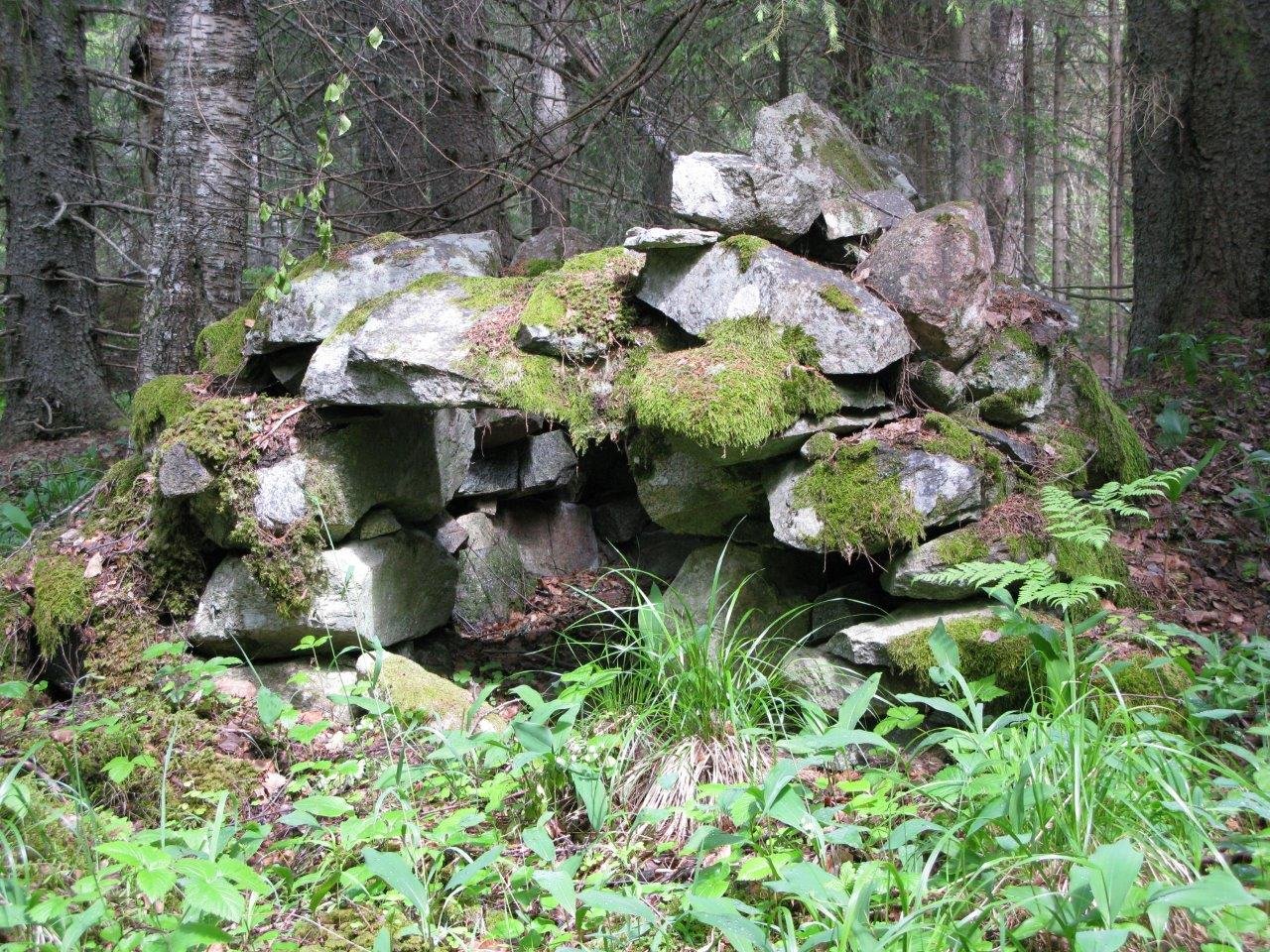 I skogen ligger en hög med mossklädda större stenar.