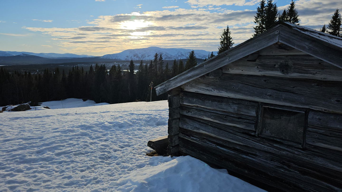 Utsikt mot ett fjäll med en fäbod i framkanten 