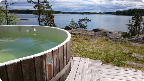 En badtunna står på ett trädäck. Från badtunnan ser man hav och skog.
